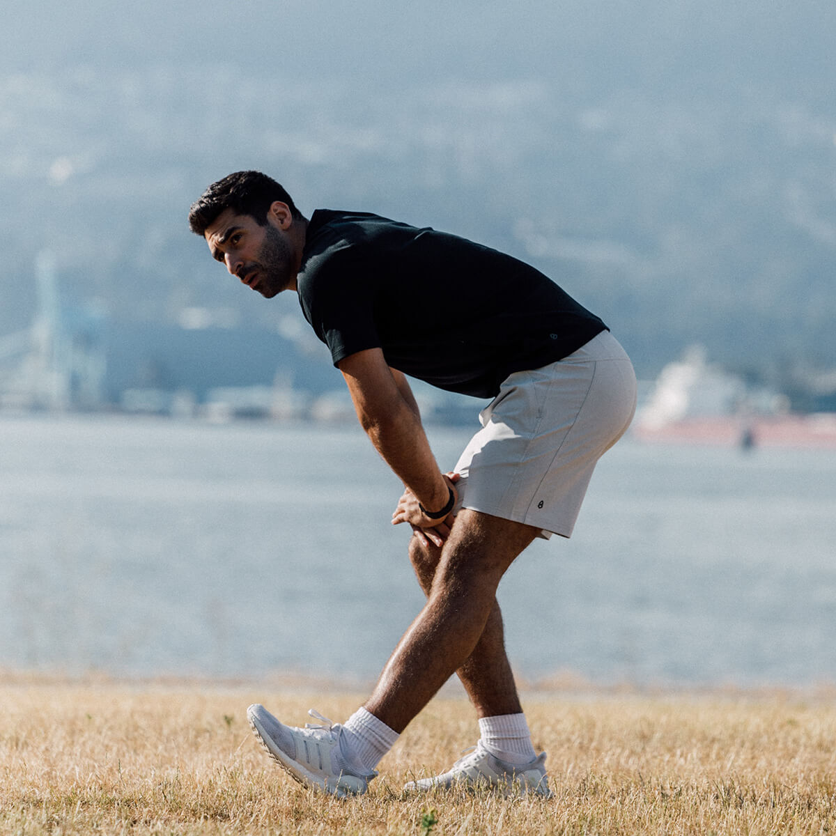 Man stretching in white athletic shorts in a field with a city beyond