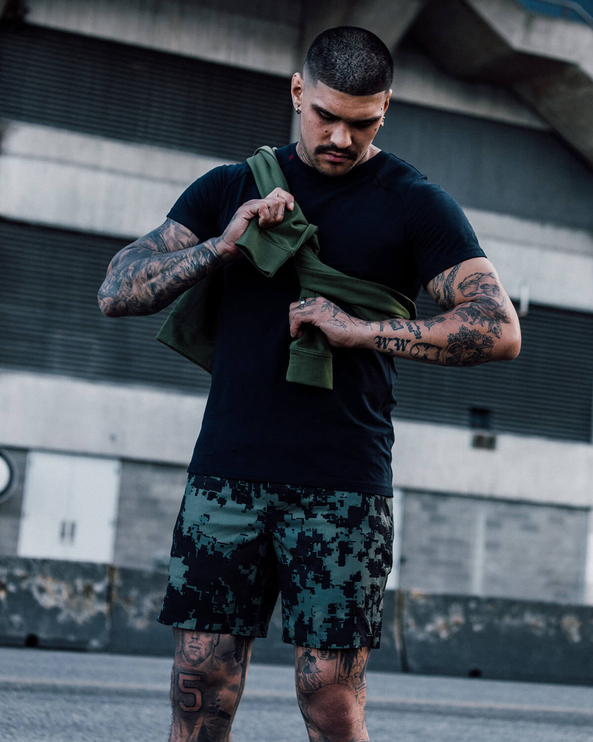 Man in camo training shorts in the city with a sweater draped around his shoulders
