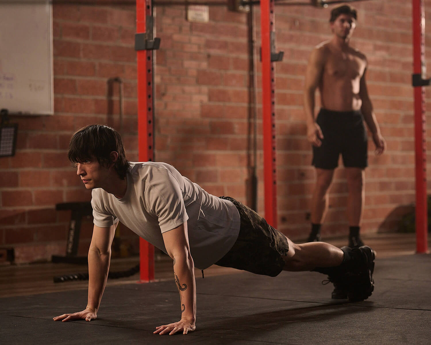 Athletic man doing a pushup in Black Crest light grey shirt and camo training shorts